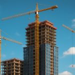 Construction site featuring multiple cranes and a tall building under development against a blue sky.