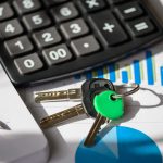 Close-up of keys on a desk with a calculator and financial documents.